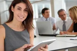 Conseillère souriante tenant une tablette, collègues en réunion à l'arrière-plan